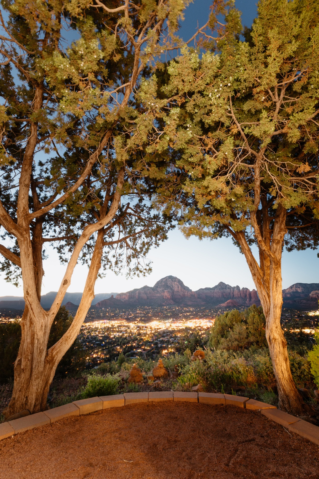 Twilight view of Sedona's red rocks and city lights framed by juniper trees from the Sky Ranch Lodge overlook