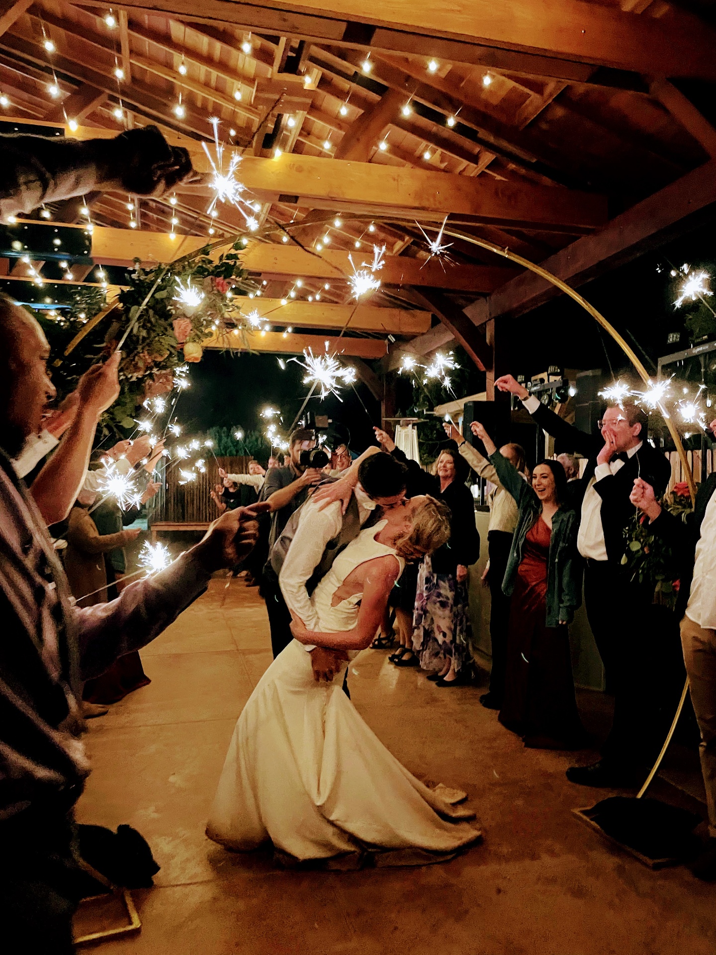 Bride and groom kissing under a gold arch during a sparkler exit inside the Sky Ranch Lodge pavilion