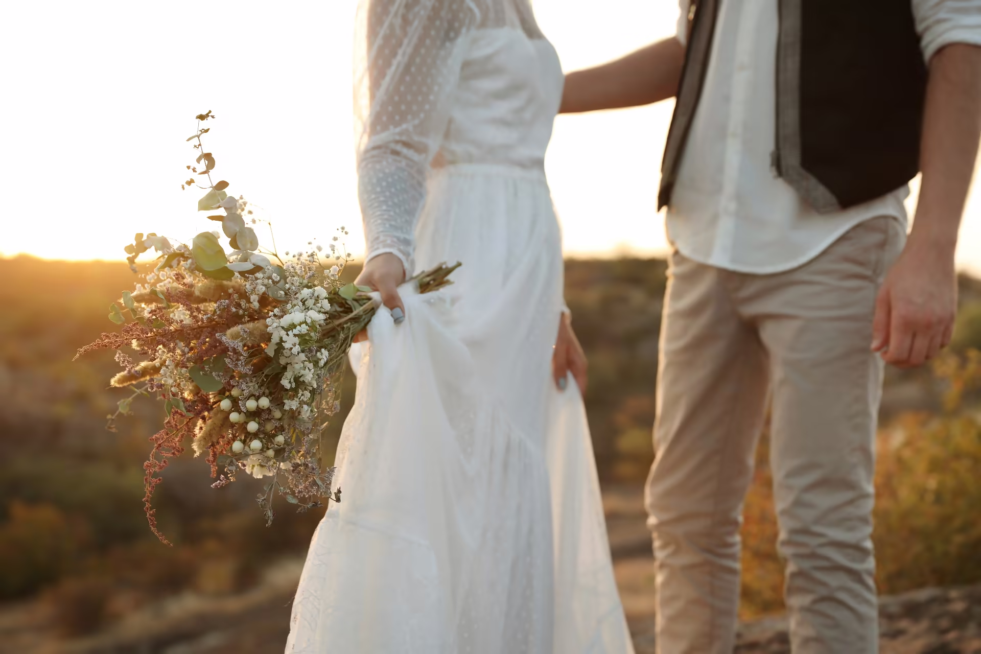 Happy newlyweds with a beautiful wildflower bouquet outdoors at golden hour